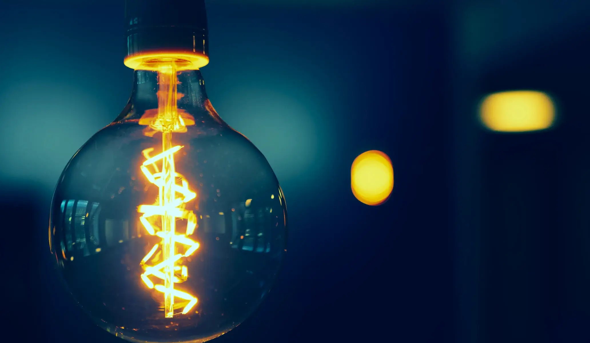 Close-up of a glowing vintage Edison filament light bulb against a dark blue background